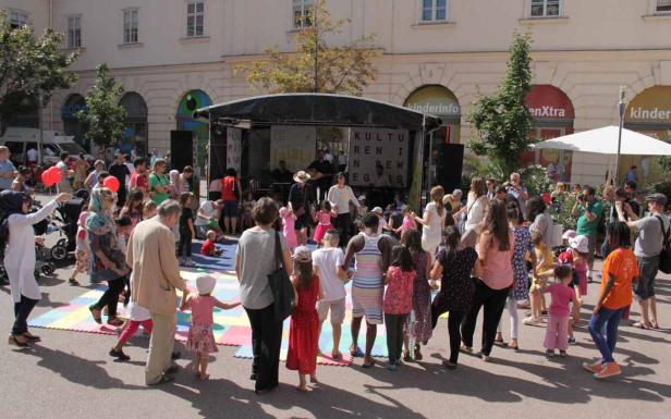 Eine Gruppe von Menschen, darunter viele Kinder, tanzt vor einer Bühne bei einer Veranstaltung im Freien.