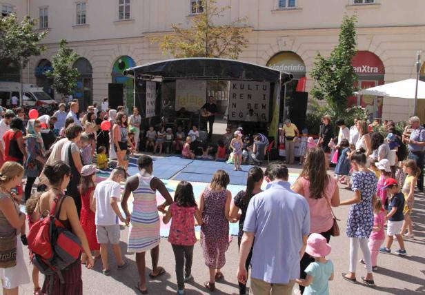 Eine Gruppe von Kindern und Erwachsenen versammelt sich vor einer Bühne im Freien.