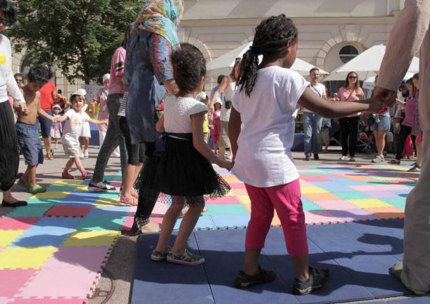 Kinder und Erwachsene tanzen Hand in Hand auf einer bunten Matte.