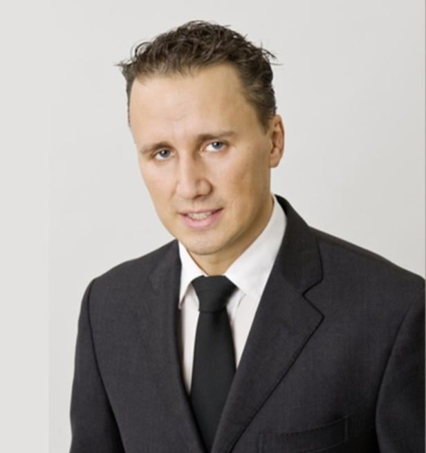 Ein Mann im Anzug mit Krawatte vor einem neutralen Hintergrund.
