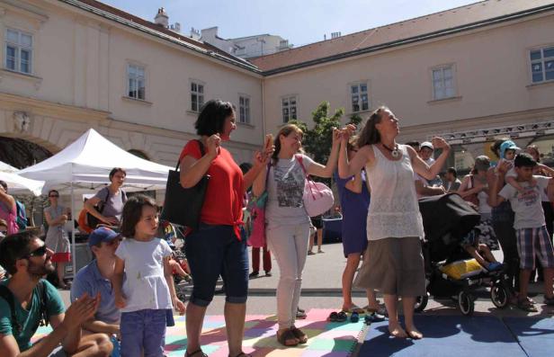 Eine Gruppe von Menschen tanzt barfuß auf einer Bühne im Freien.
