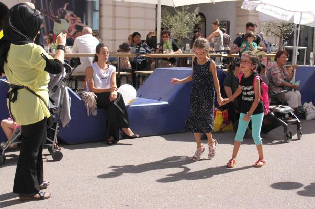 Zwei Mädchen mit Gesichtsbemalung tanzen Hand in Hand auf einer belebten Straße.