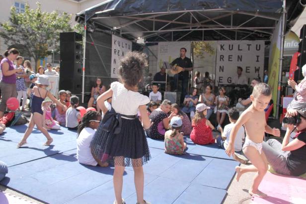 Kinder tanzen und spielen vor einer Bühne bei einer Kulturveranstaltung.