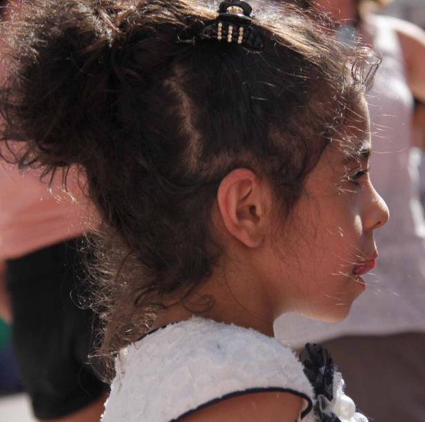 Ein Mädchen mit dunklen Locken und einem weißen Kleid im Profil.