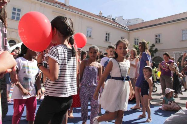 Eine Gruppe von Kindern versammelt sich im Freien mit roten Luftballons.