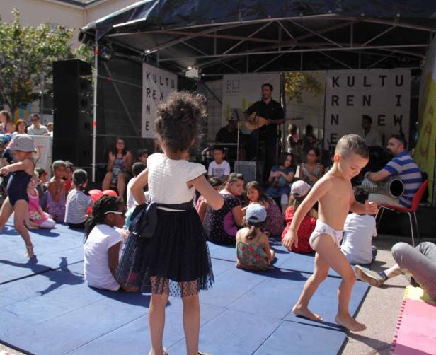 Kinder tanzen barfuß auf einer Bühne vor einer Band bei einer Kulturveranstaltung.
