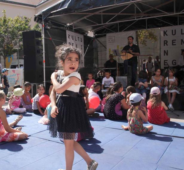 Ein junges Mädchen tanzt vor einer Bühne, auf der eine Band spielt, während andere Kinder zusehen.