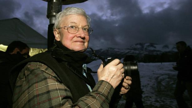 Ein älterer Mann mit Brille fotografiert in einer winterlichen Landschaft.