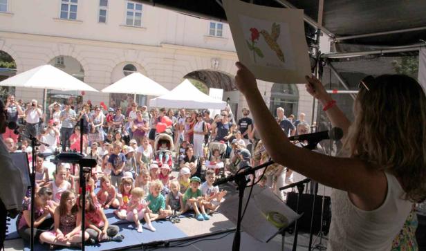 Eine Frau präsentiert vor einer Gruppe von Kindern eine Zeichnung eines Kolibris.