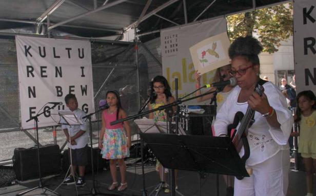 Eine Frau spielt Gitarre, während Kinder auf einer Bühne singen.