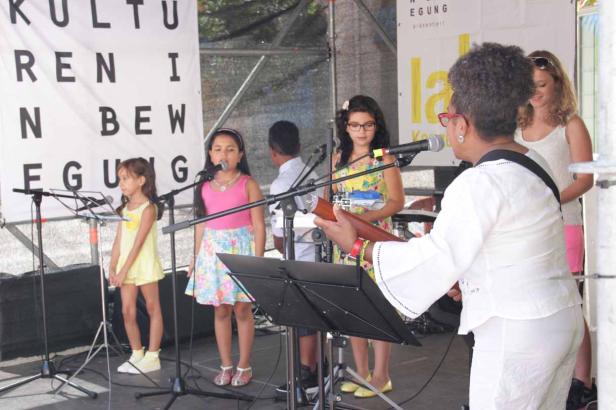 Eine Musikgruppe tritt mit Sängerinnen und Gitarristin auf einer Bühne auf.