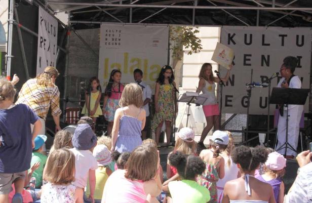 Eine Gruppe von Kindern tritt mit zwei Frauen auf einer Bühne auf.