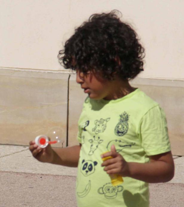 Ein Junge mit lockigem Haar pustet Seifenblasen.