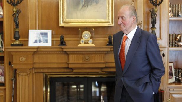 Juan Carlos I. in einem blauen Anzug vor einem Kamin.