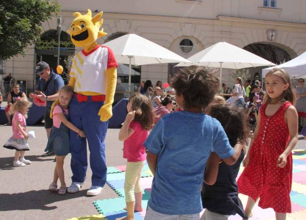 Ein gelbes Maskottchen steht mit einer Gruppe von Kindern im Freien.