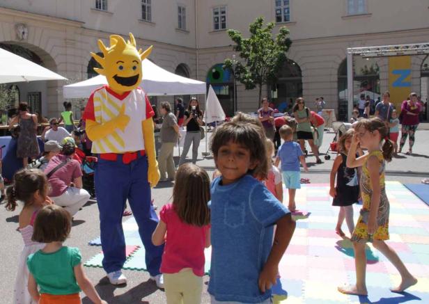 Kinder spielen mit einem Maskottchen auf einer Veranstaltung im Freien.