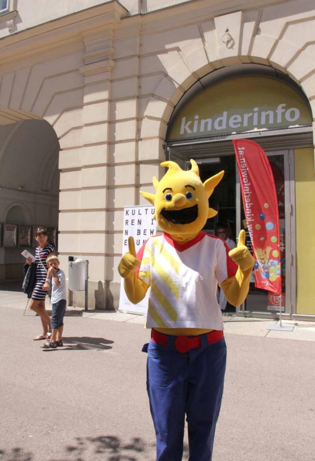 Ein gelbes Sonnenmaskottchen steht vor einem „Kinderinfo“-Laden.