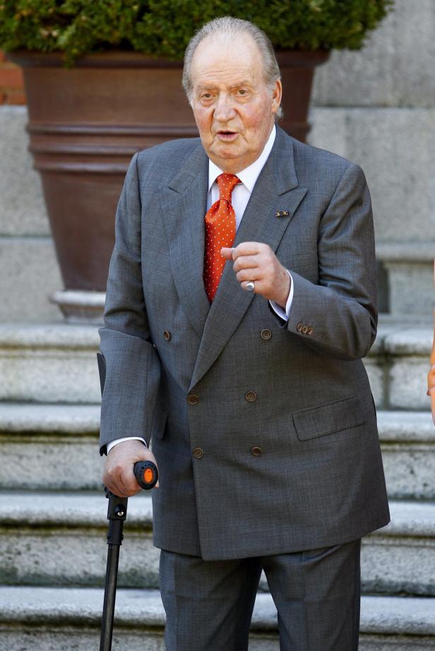 Juan Carlos I. mit Anzug und Gehstock vor einer Treppe.