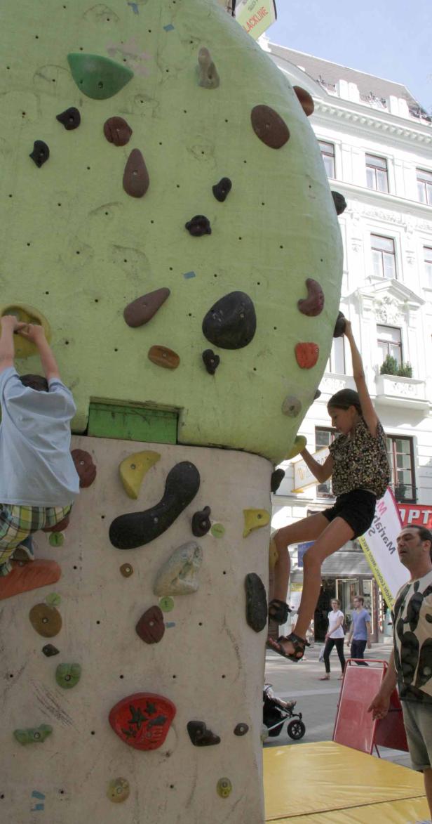 Ein Mädchen klettert an einer künstlichen Kletterwand im Freien.