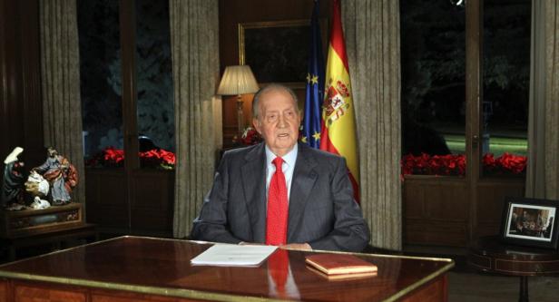 Juan Carlos I. sitzt an einem Schreibtisch vor der spanischen und der EU-Flagge.