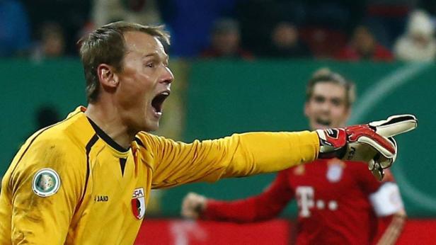 Ein Torwart in gelbem Trikot gestikuliert und schreit auf dem Fußballfeld.