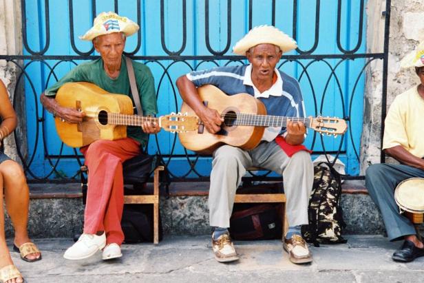 Zwei ältere kubanische Männer spielen Gitarre vor einem blauen Gebäude.