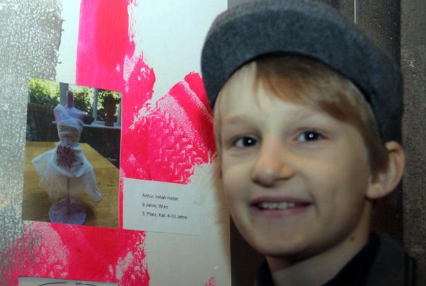 Ein Junge mit Schirmmütze steht vor einer Collage mit dem Namen Arthur Jonah Heller.