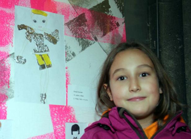 Ein junges Mädchen steht vor einer Wand mit Kunstwerken.