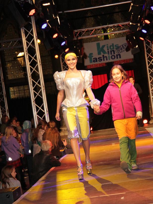 Eine junge Frau und ein Mädchen laufen Händchen haltend auf einem Laufsteg.