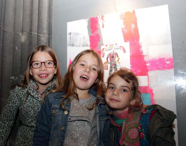 Drei junge Mädchen posieren vor einem farbenfrohen Kunstwerk.