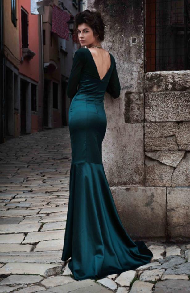 Eine Frau in einem smaragdgrünen Kleid posiert in einer Gasse.