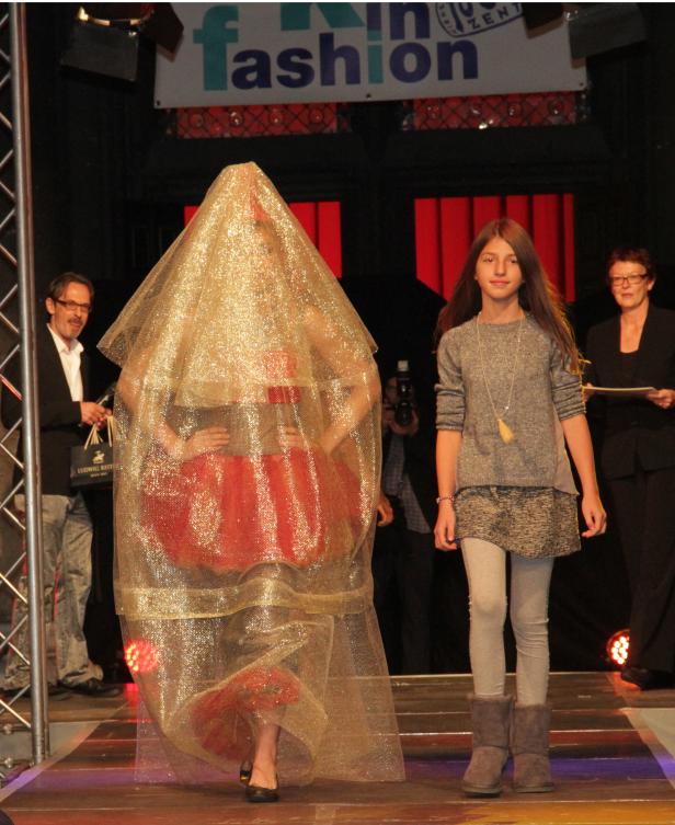 Eine Modenschau mit einem Model in einem goldenen Schleier und einem roten Kleid.