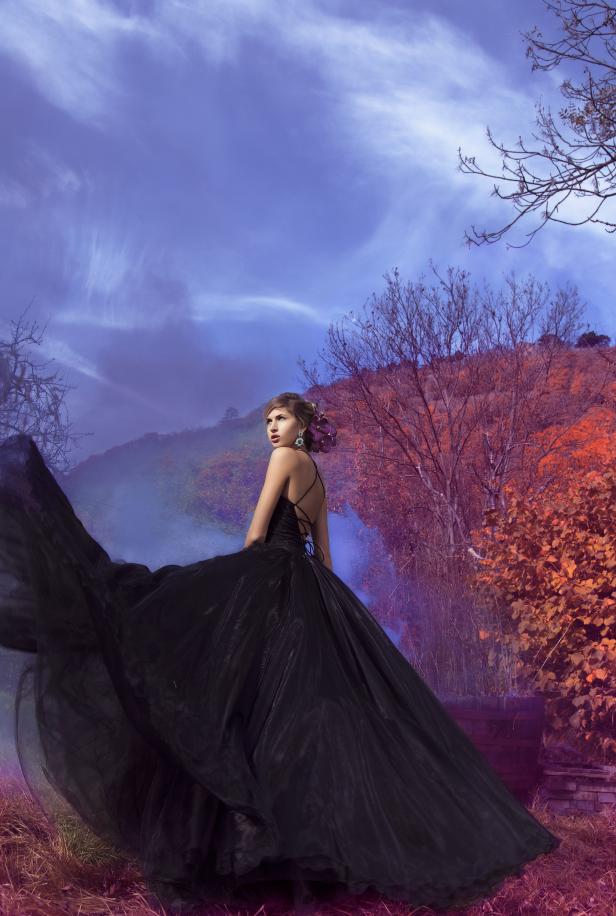 Eine Frau in einem schwarzen Kleid steht in einer surrealen Landschaft.