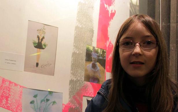 Ein junges Mädchen steht vor einer Wand mit Kunstwerken.