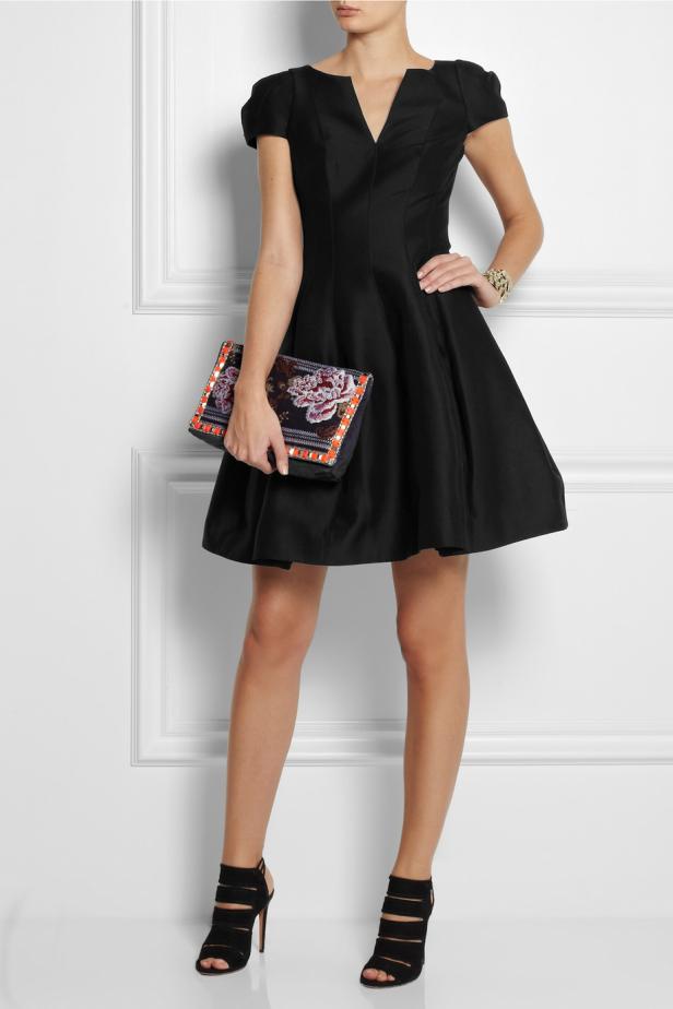 Eine Frau in einem schwarzen Kleid hält eine verzierte Handtasche.