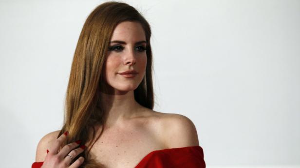 Lana Del Rey in einem roten Kleid posiert vor einem weißen Hintergrund.