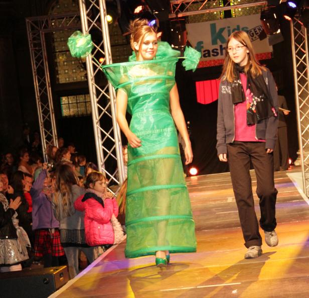 Ein Mädchen in einem grünen Kleid aus Plastik auf einem Laufsteg.