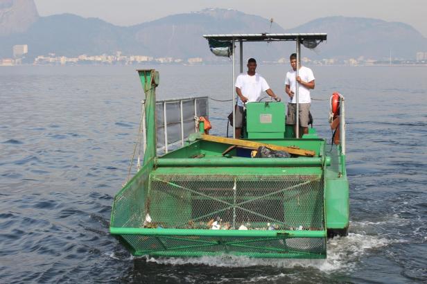 Zwei Männer bedienen ein grünes Boot, das Müll aus dem Wasser fischt.