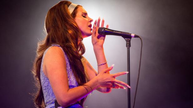 Lana Del Rey singt mit einem weißen Stirnband in ein Mikrofon.
