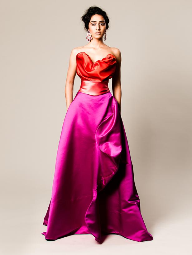 Eine Frau in einem formellen, trägerlosen Kleid mit rotem Oberteil und pinkfarbenem Rock posiert.