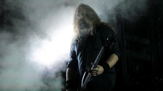 Ein Mann mit langem Haar und Bart spielt Bassgitarre im Nebel.