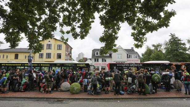 Eine Gruppe von Menschen mit Rucksäcken wartet vor Bussen in einer Stadt.