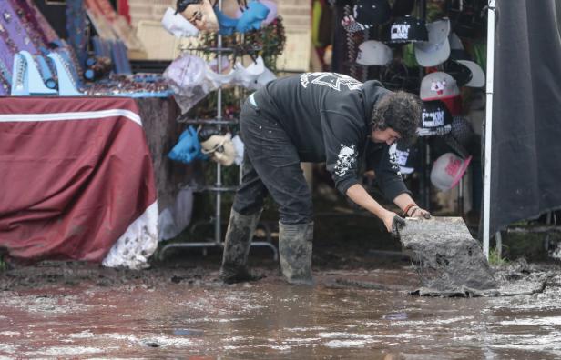 Eine Person in Gummistiefeln hantiert mit einer schlammigen Plane auf einem Festivalgelände.