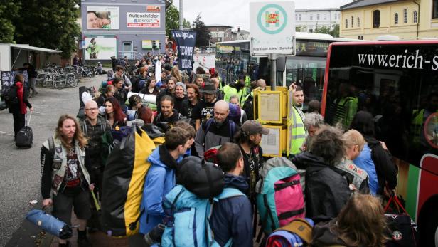 Eine große Gruppe von Menschen mit Gepäck wartet an einer Bushaltestelle, möglicherweise auf dem Weg zu einem Festival.