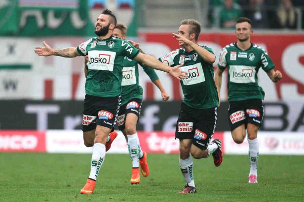 Mehrere Fußballspieler in grünen Trikots jubeln auf dem Spielfeld.