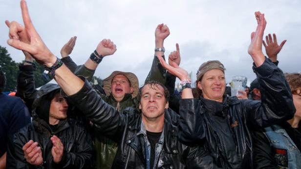 Eine Gruppe von Menschen jubelt mit erhobenen Händen auf einem Festival im Regen.