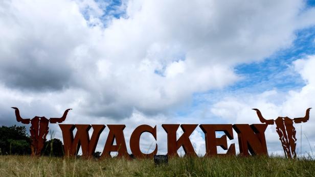 Das Wacken-Logo mit zwei stilisierten Bullenschädeln auf einem Feld unter bewölktem Himmel.
