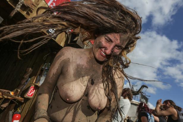 Eine lächelnde, schlammbedeckte Frau mit fliegenden Haaren vor blauem Himmel.