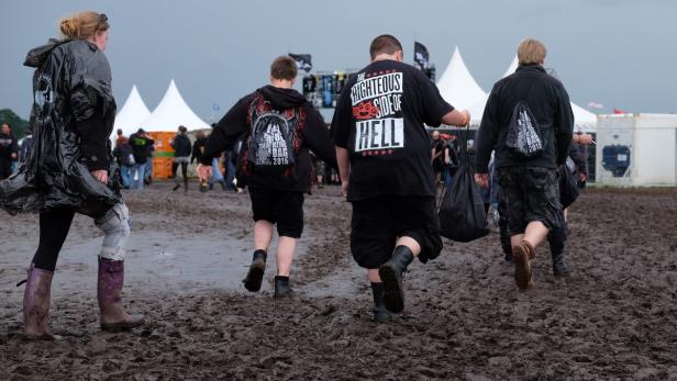 Mehrere Personen waten durch den Schlamm auf einem Festivalgelände.