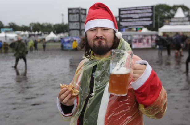 Ein Mann im Weihnachtsmannkostüm hält ein Bier und einen Burger auf einem Festivalgelände.